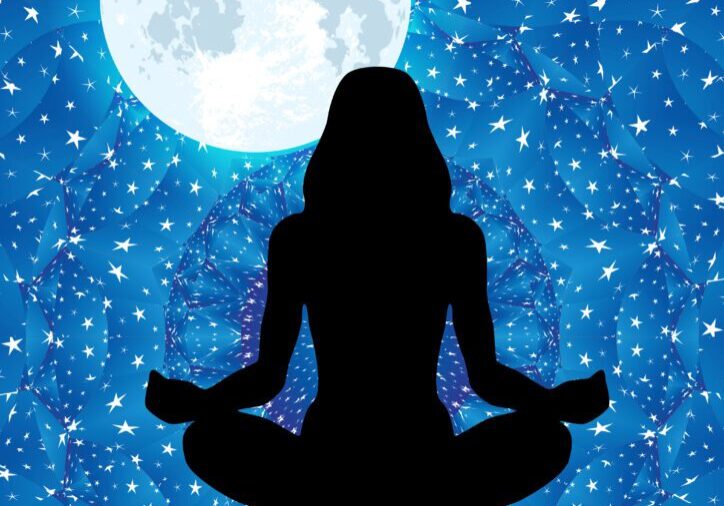 Woman’s silhouette meditating under the moon with mandala background